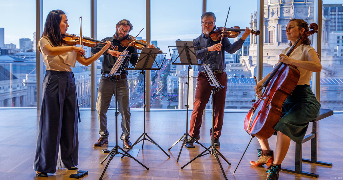Del Sol Quartet performing in front open windows showing a city skyline.